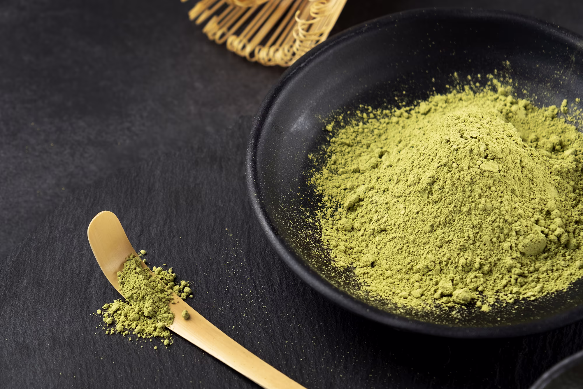 Bright green matcha powder with a bamboo whisk